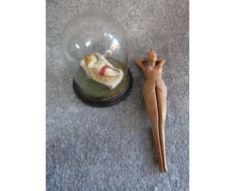 A wax model of a female figure on a chaise longue in an antique glass dome and a wooden nut cracker in the form of a reclinin