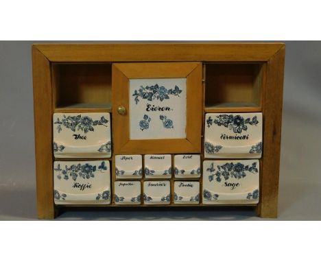 A vintage Dutch herb and spice cabinet with ceramic drawers and door and wooden frame. Central cupboard has holes for storing