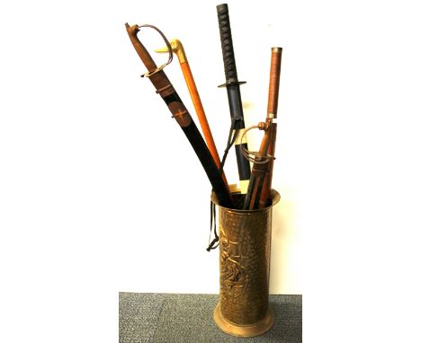 A group of four mixed swords and a walking stick in a brass stick stand.