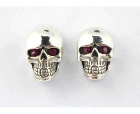 A pair of 925 silver skull shaped stud earrings with ruby set eyes, L. 1.3cm.