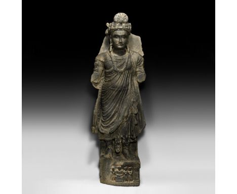 3rd-4th century AD. A carved schist statue of bodhisattva Maitreya standing with loosely draped clothing and swags of beads, 