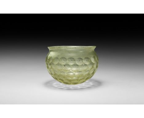 3rd-7th century AD. A squat pale green glass cup with rounded base and everted rim, seven bands of wheel-cut facets to the ou