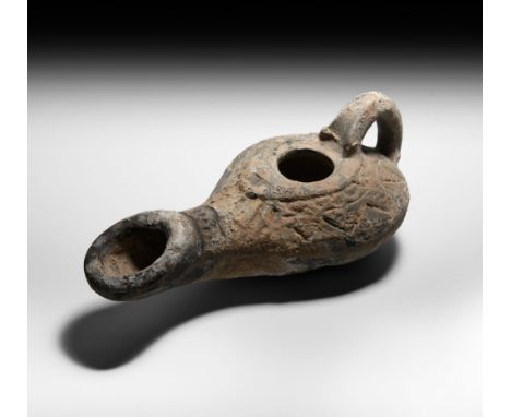2nd century BC-2nd century AD. A substantial ceramic slipper-shaped oil lamp with strap handle and large flared and elongated