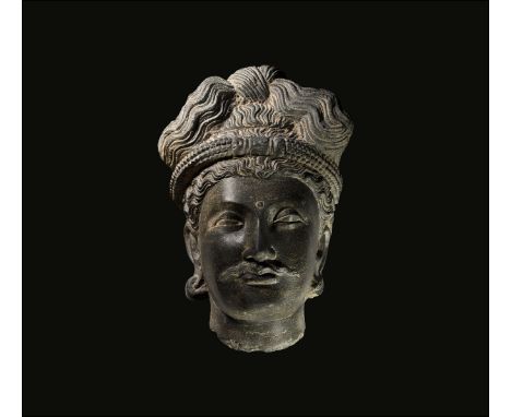 2nd-3rd century AD. A carved schist head of a bodhisattva with elaborate knotted hairstyle, beaded band to the brow and urna 