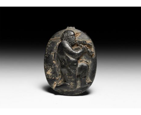 1st century BC-1st century AD. A discoid bone panel with high-relief image of Silenus kneeling nude with cloak over one shoul