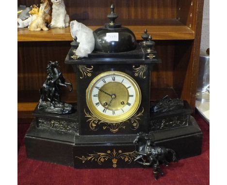 A late-19th century black slate striking mantel clock surmounted on the sides by a pair of spelter Marly Horses above a raise
