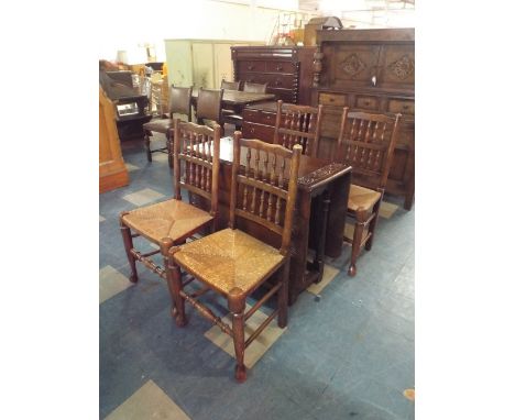 An Oak Drop Leaf Gate Legged Dining Table with Carved Border and Four Rush Seated Spindle Back Dining Chairs 