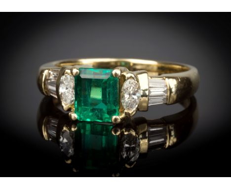 An 18ct yellow gold, Columbian emerald and diamond ring, the 1ct emerald cut Columbian emerald flanked by two eliptical cut d