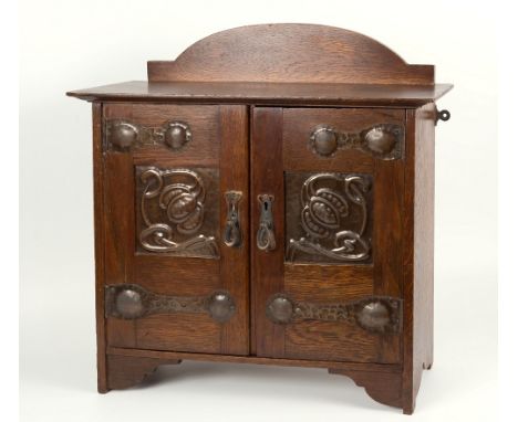 An Arts and Crafts oak wall cabinet, with decorative worked copper panels, ornate hammered copper hinges to doors, original l