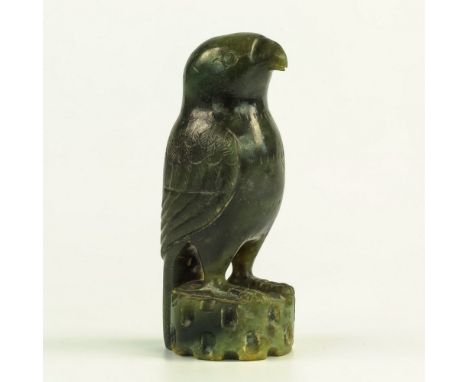 A Chinese carved spinach jade figure of a falcon, probably 19th century, archaistic in form, in upright stance upon an indent