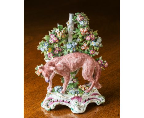 A Bow porcelain candlestick, 18th century, modelled as a fox seeking prey in front of a bocage background, on scrolled polych