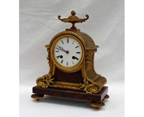 A 19th century ormolu and variegated red marble mantle clock, with an urn finial above a domed leaf cast top scrolling sides,