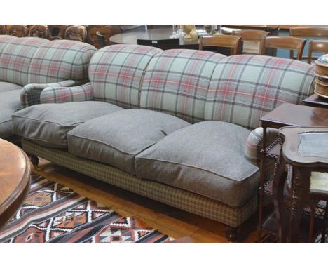 A three seater sofa, upholstered in a green tartan and tweed, with loose cushioned seat, raised on turned legs moving on bras