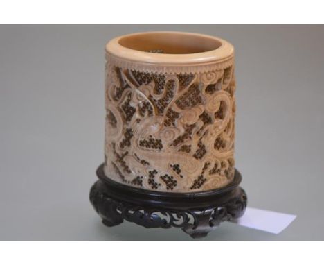 A Chinese tusk section ivory brush pot, Canton, 19th century, carved in relief with dragons against a pierced ground, lacking