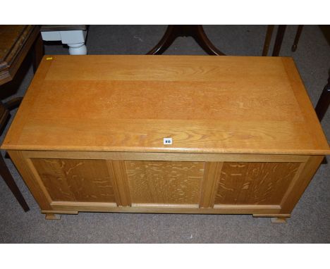 A modern oak blanket box with triple panel front and hinged cover, raised on bracket feet.