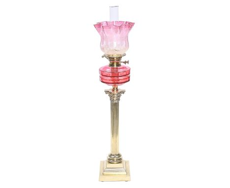 An Edwardian brass Corinthian column oil lamp, with cranberry glass fount, brass burner and an etched and cranberry tinted gl