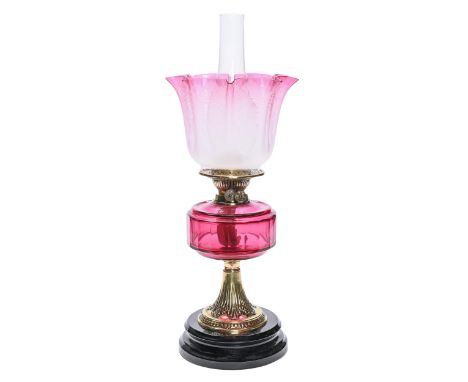 A late Victorian brass oil lamp, on black glazed pottery foot, with cranberry glass fount, brass burner and an etched and cra