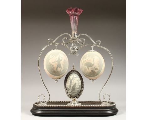 A SUPERB AUSTRALIAN CENTREPIECE, a plated stand with three carved emu egg; aborigine, emu and kangaroo, with ruby glass flowe
