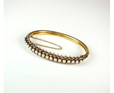 A late 19th century untested pearl hinged bangle, designed as a row of eighteen split pearls set to stylised plaited mount wi