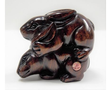Japanese carved wood Netsuke modelled as a form of pair of mating rabbits, signed to circular bone tablet, length 4cm.