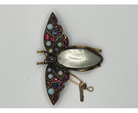 An Arts and crafts style moth brooch featuring a mother of pearl body and wings adorned with opals, sapphires and rubies of v