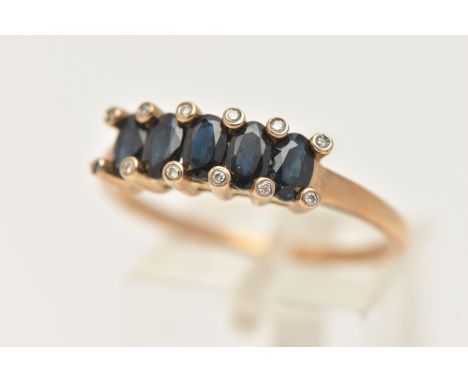 A 9CT GOLD SAPPHIRE AND DIAMOND RING, designed as a row of five oval cut deep blue sapphires, shared four claw settings with 