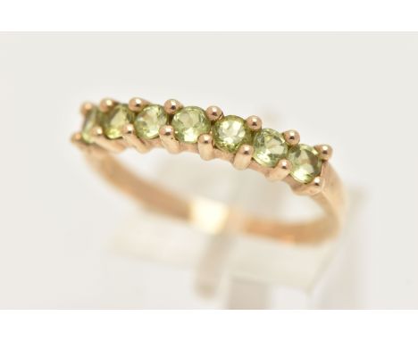 A 9CT GOLD SEVEN STONE RING, set with seven circular cut green stones believed to be peridot, each in a claw setting, to a po