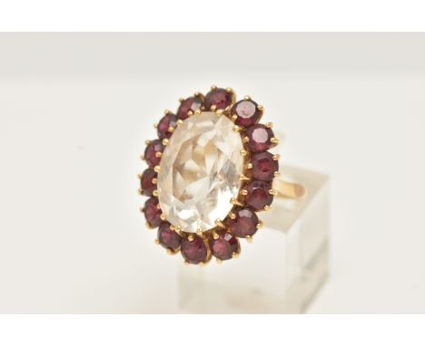 A YELLOW METAL ROCK CRYSTAL AND GARNET CLUSTER RING, set with an oval shape rock crystal, measuring approximately 18.04mm by 