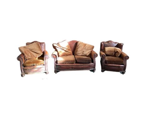 A Brown Leather Three Piece Suite, early 20th century, comprising a two seater sofa and two matching armchairs, with scroll o