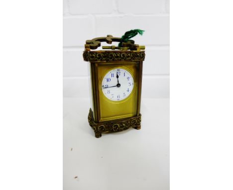 A small brass cased carriage clock with glass panels between scroll frieze decoration to top and bottom, with a shaped loop h