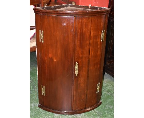 A George III mahogany bow-fronted wall hanging corner cupboard, moulded top above a pair of concave doors, enclosing a pair o