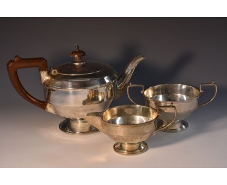 A George V silver three piece pedestal tea service, comprising teapot, milk jug and sugar basin, scroll-capped handles, the t