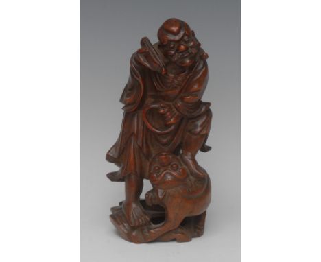 A 19th century Chinese bamboo carving, of a deity, holding a scroll and quoit, wearing flowing robes, one foot standing on th