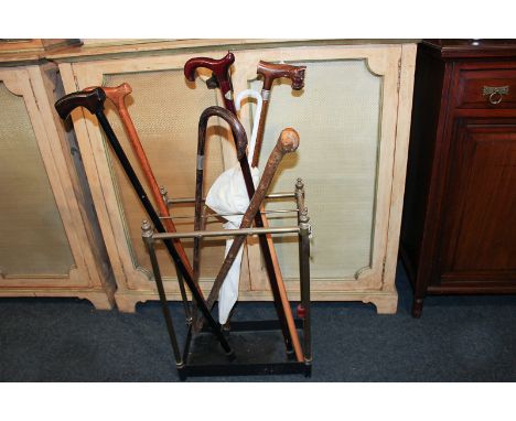 A brass stick stand of six sections, together with an assortment of walking sticks including two with carved dog head handles