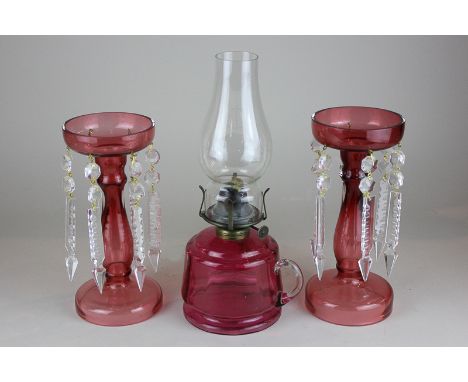 A cranberry glass oil lamp with clear glass funnel, together with a pair of cranberry glass candlesticks with clear glass dro