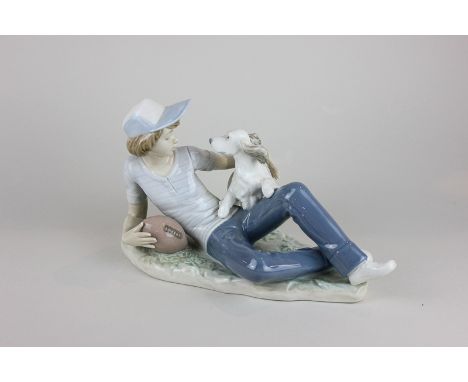 A Nao porcelain figure of a boy reclining with a rugby ball and a spaniel, 16cm high