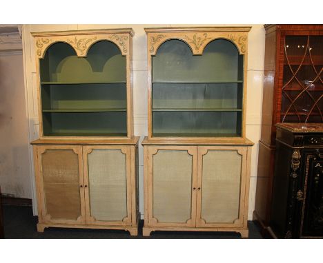 A pair of Italian bookcase cabinets, painted in cream and green, with three open shelves above two glazed brass grille doors 