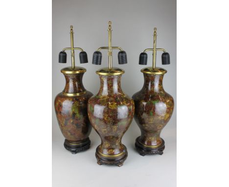 A pair of cloisonne vase lamps together with a similar lamp, floral decoration on red ground, all three on hardwood stands
