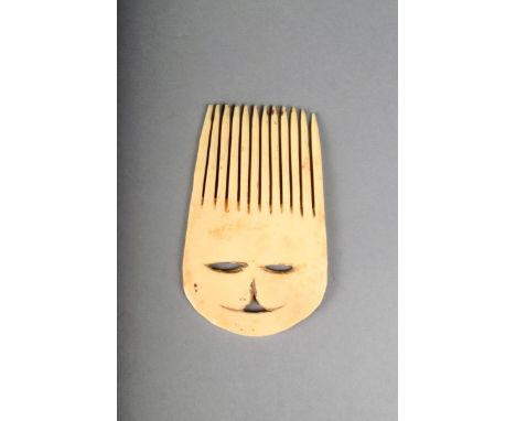 An Inuit carved bone comb, with pierced facial features, 10.5cm high.