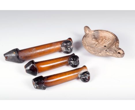 A Roman pottery oil lamp, the centre moulded an erotic scene, 10.5cm long and three glass phallic vessels. (4)