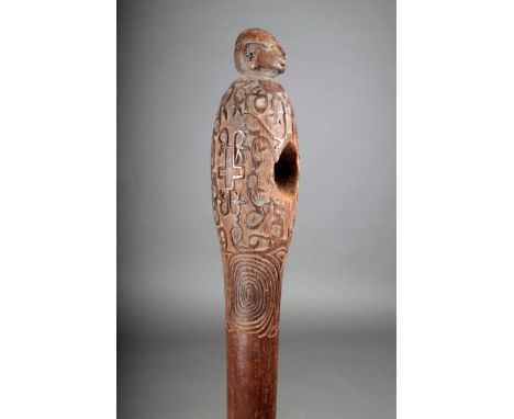 An Asmat axe handle, Papua, carved with a head finial and relief decoration with a tapering handle with a bird head and open 