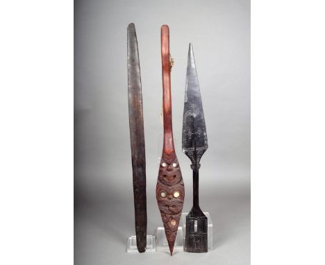 A Maori ornamental hoes, carved tiki masks with inlaid shell, 77.5cm long, a Massim carved wood ornamental dagger, 71cm long 