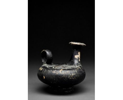 Ca. 360-320 BC A ceramic black-glazed guttos with discoid body, pedestal foot, loop handle and trumpet-shaped spout; circumfe
