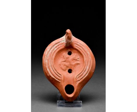 Ca. 1-200 AD A terracotta oil lamp with a ring base, smooth side walls, grooved perimeter, and a recessed tondo decorated wit