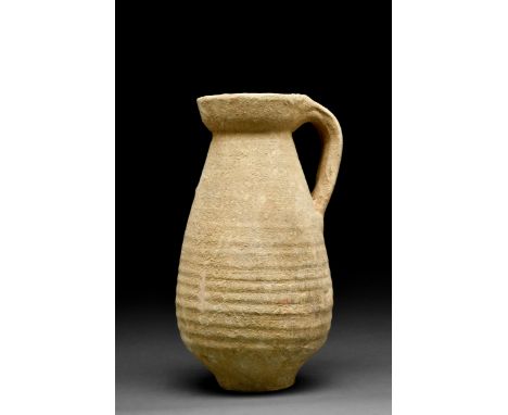 Ca. 1-400 AD An unglazed ceramic tall piriform jug with spiral wheel-ridging, broad mouth, sturdy strap handle connecting rim