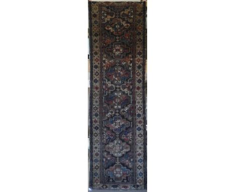 A Caucasian runner, the central panel set with repeating medallions on a dark brown ground, within a stepped cream, brown, bl