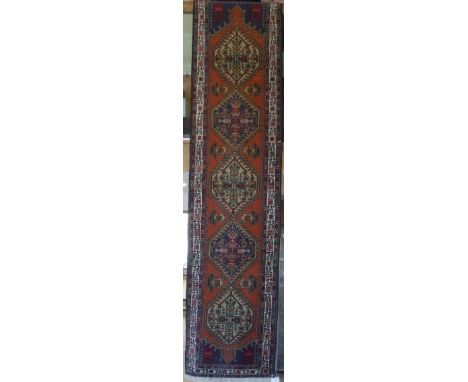 A Persian runner, the central panel set with repeating lozenge shaped medallions on a terracotta ground within a stepped blue