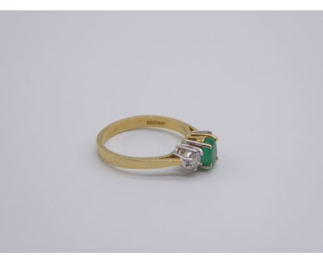 An 18ct yellow gold ring set with a dahlia cut Emerald flanked by two diamonds, 3g,