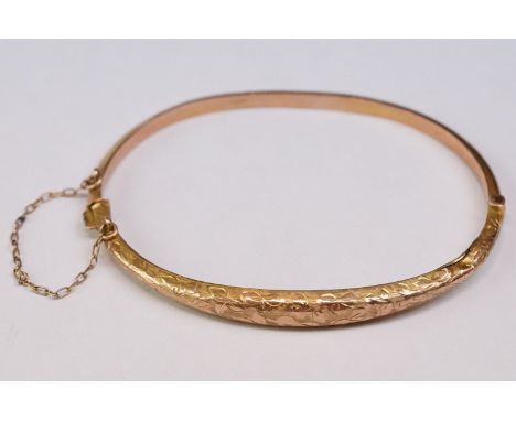 9ct rose gold hinged bangle, engraved foliated design to tapered upper half, tongue and box clasp with safety chain 