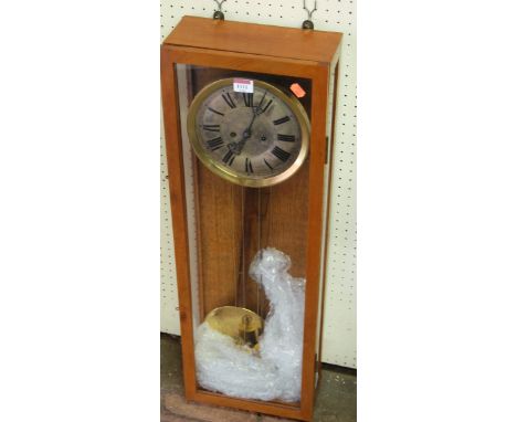 A mid 20th century teak cased drop trunk wall clock having a silvered circular 8" dial with twin winding holes, pendulum and 